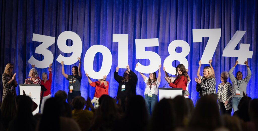 Delta Gamma members help announce the current amount raised. They are on stage holding up 3 foot tall numbers that say "39,015,875"
