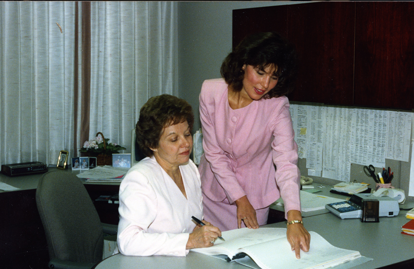 Photo of two women at a desk, one is signing a paper