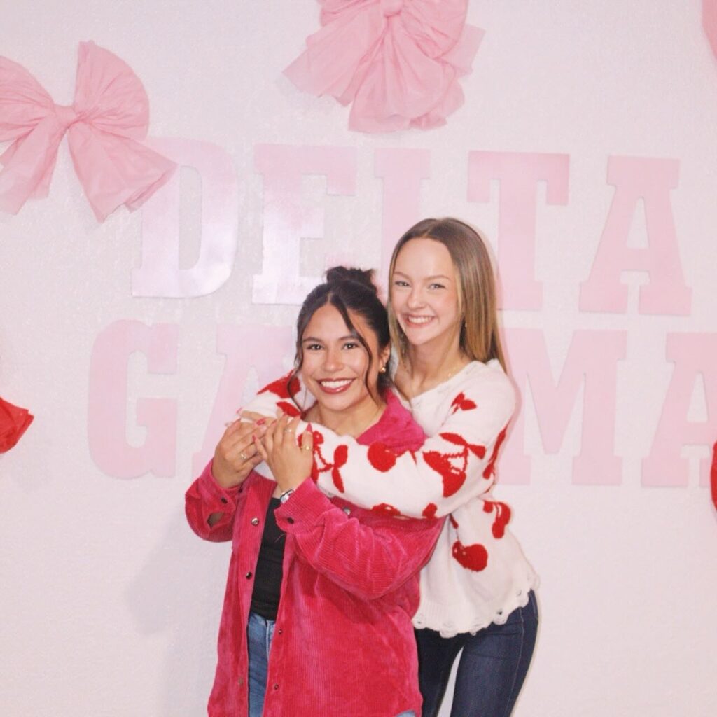 Two girls posing in front of a large pink Delta Gamma backdrop
