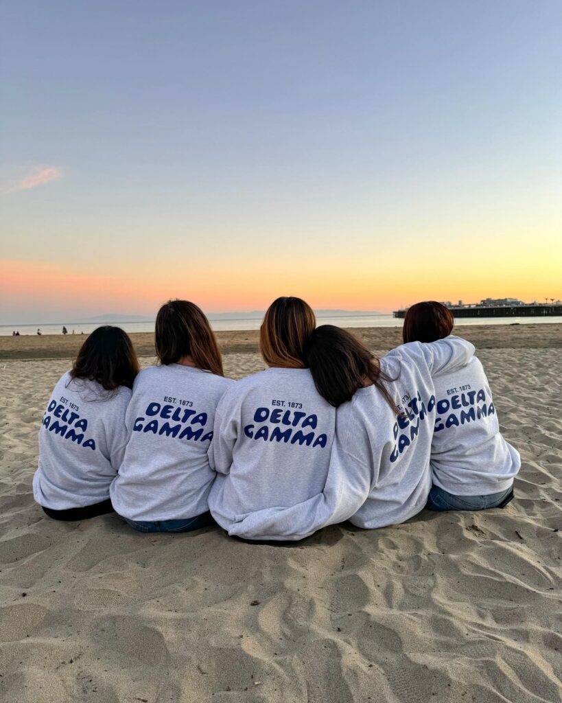 A group of girls sitting on the sand on a beach looking out into the ocean