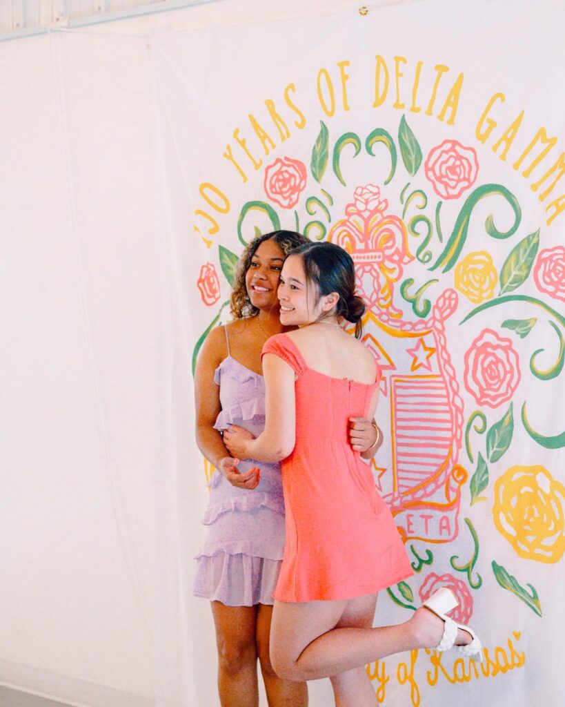 Two girls in front of a pink backdrop smiling for a picture