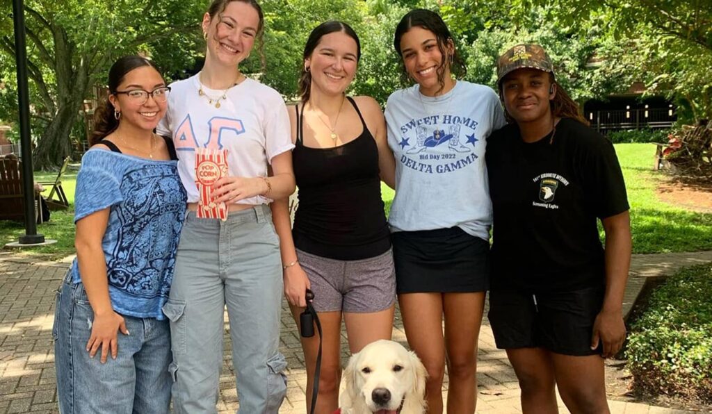 Group of girls posing for photo with dog in front
