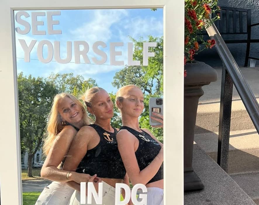 Three girls taking a photo in front of mirror that says See Yourself in DG
