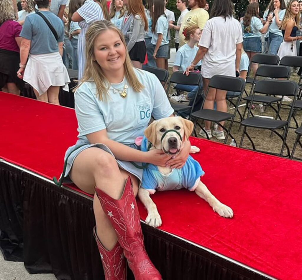 DG member sitting next to service dog on red stage