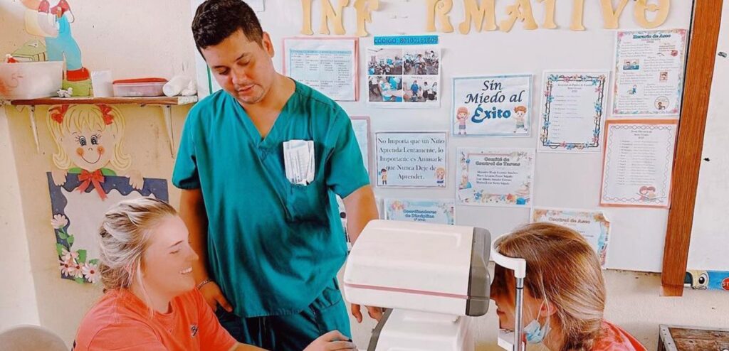 Doctor or a nurse helping a volunteer read eye machine as another girl looks through machine