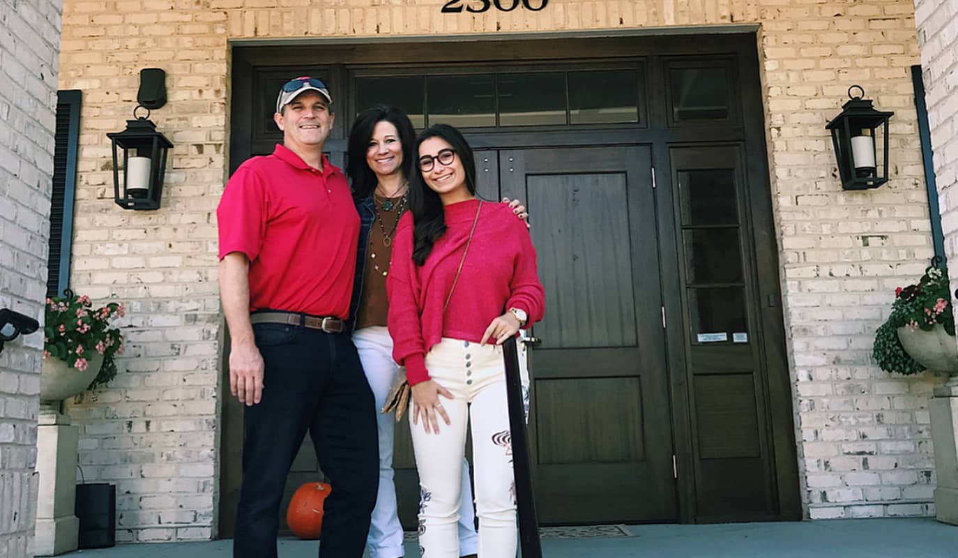 Family of three dressed in red, standing in front of Delta Gamma house
