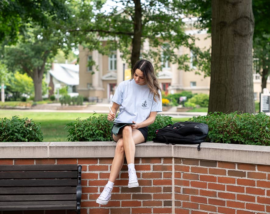 Girl sitting on brick wall writing on iPad
