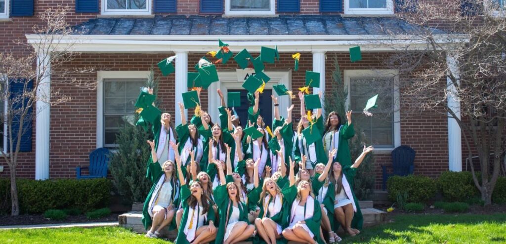 DG Graduates throwing caps into the air in front DG House