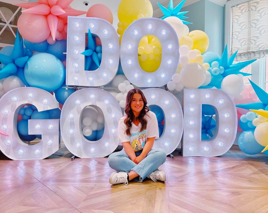 Young girl sitting in front of Do good Light up sign and balloons