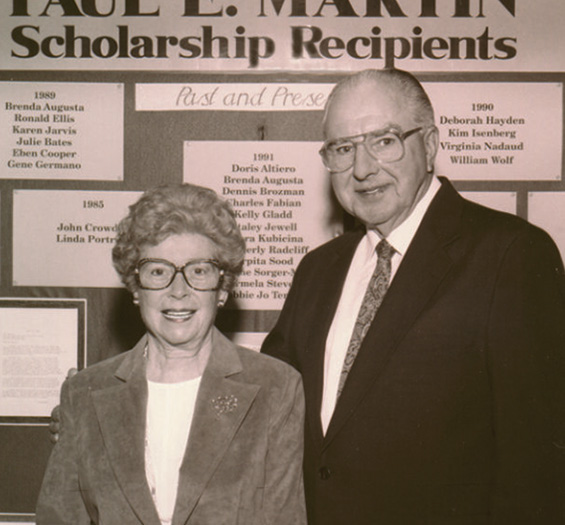 A black and white photo of Paul and Dorothy Martin. They are standing in front of a sign that says "Paul E Martin Scholarship Recipients"