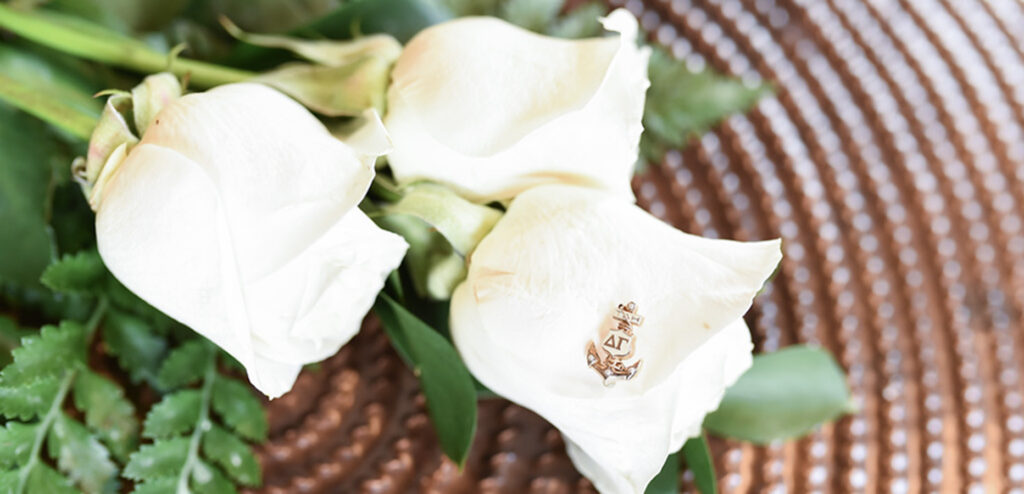 Three white roses rest on their sides, with a Delta Gamma badge set gently on one rose.