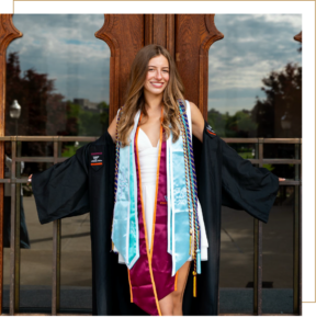 Julia poses in her graduation regalia in front of a wooden door with glass windows.