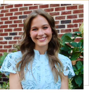 Avery is standing outside in front of a brick wall and wearing a blue dress.