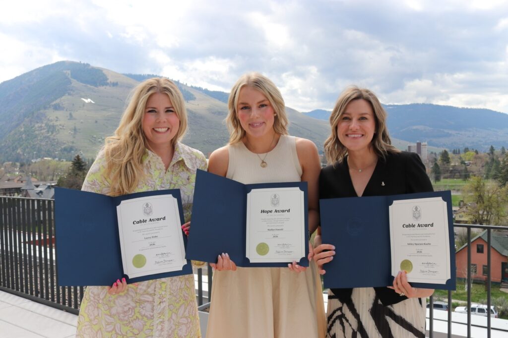 Three Pi-Montana and Missoula alumnae at Founders Day celebration holding Individual Alumnae Award folders with mountains in the background.